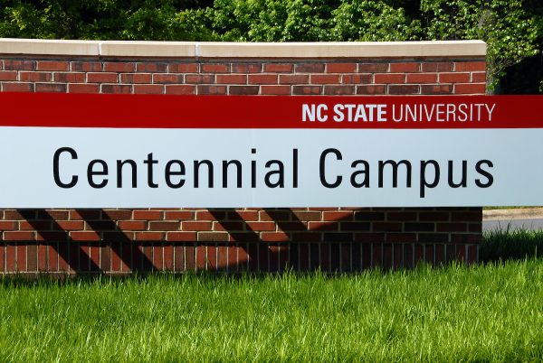 Avent Ferry entrance to Centennial Campus. NC State University is in white letters with a red background. Centennial Campus is in black letters with a white background.