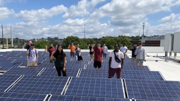 Group of students standing among rows of solar panels.
