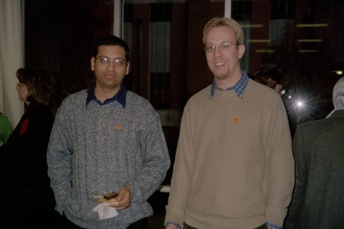 Dipankar Ghosh, left, wearing a gray sweater over a dark blue collared shirt poses with male friend who is wearing a tan sweater over a blue and white collared shirt. Both are wearing eyeglasses.