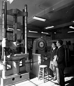 In this photo, taken around 1949, Dr. Charles R. Bramer, right, works on an investigation of wood truss member tension splices joined with split-ring connectors using the department’s universal testing machine. The photo was taken in the department’s former structures and materials lab located in “old” Mann Hall, now the east wing of Daniels Hall on North Campus.
