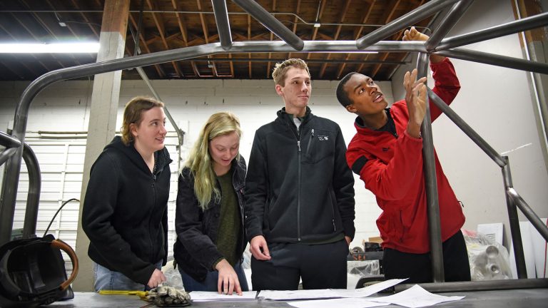 Mechanical engineering's Bryon Spells (right) points out recent welding work to SolarPack teammates while checking on the progress of their car at Eastern Rod and Customs.