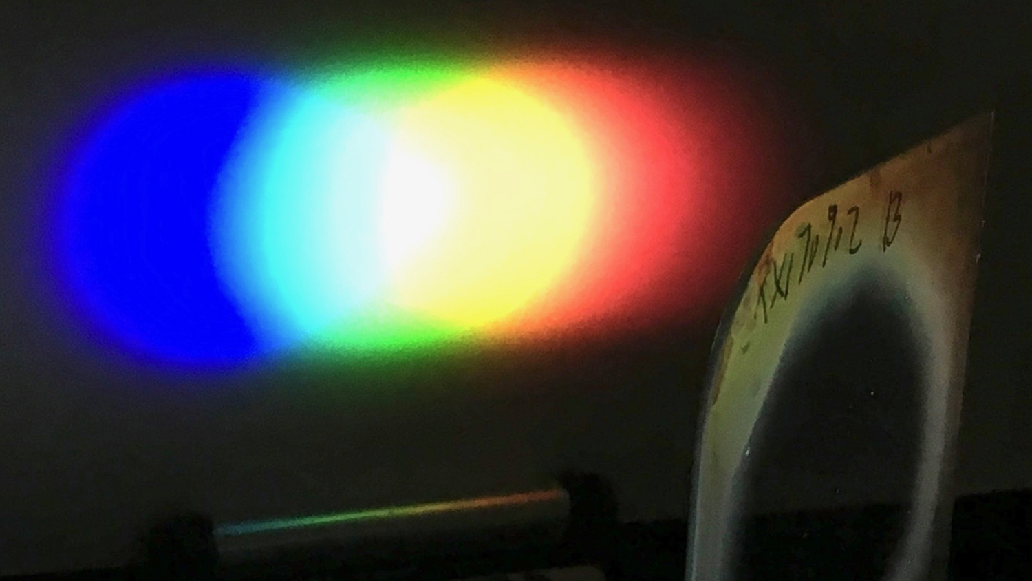 A one-inch diameter Bragg polarization grating diffracts white light from an LED flashlight onto a screen placed nearby.