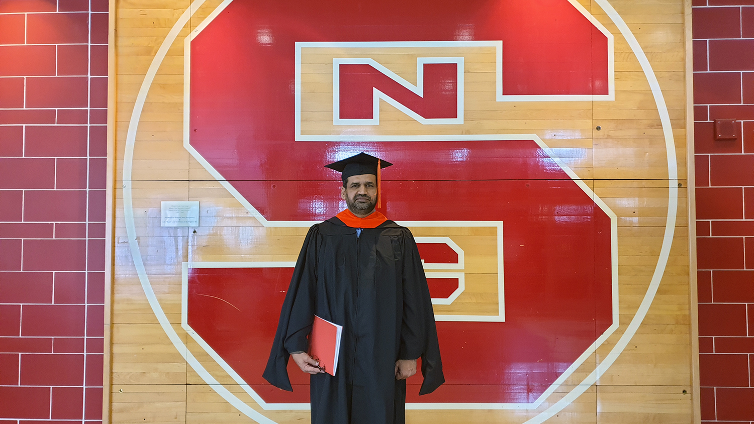 Israr Ul Haq, an Engineering Online student, poses near NC State's logo on campus.