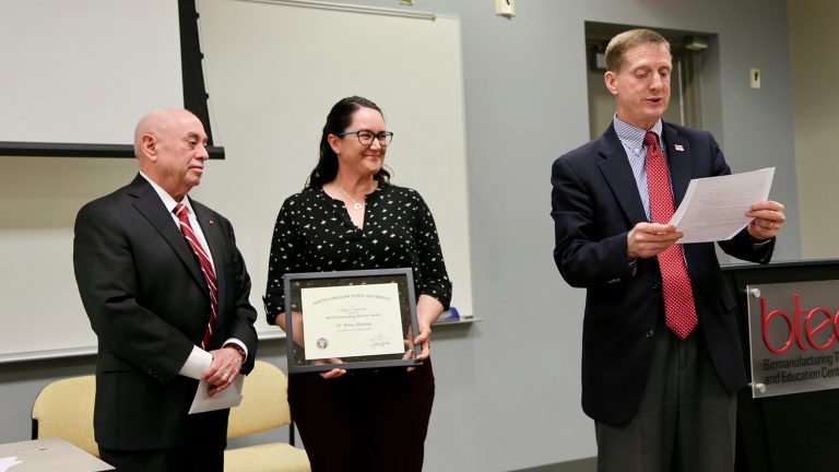Dr. Brina Montoya, center, accepts an Outstanding Teacher Award from Dr. Louis Martin-Vega while Dr. Jerome Lavelle reads her citation.