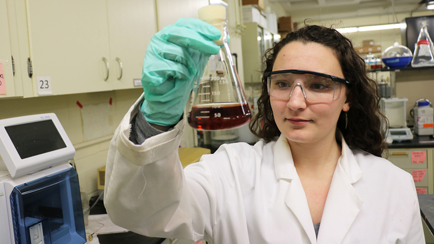 Erin Cooper examines flask in lab.
