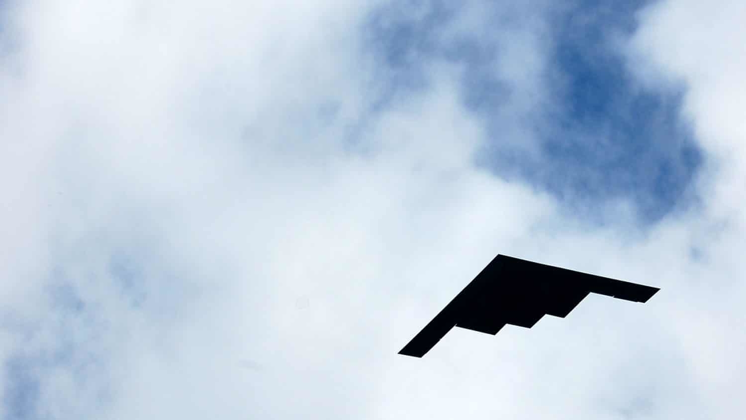 A B-2 Spirit (stealth) bomber is silhouetted against the clouds.