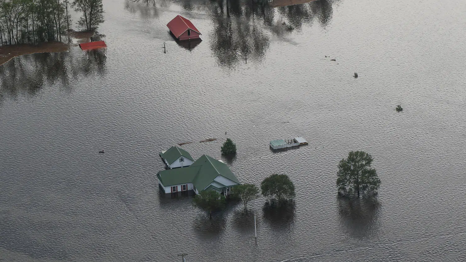 Aerial view of flood waters surrounding a house, barn and adjacent land.
