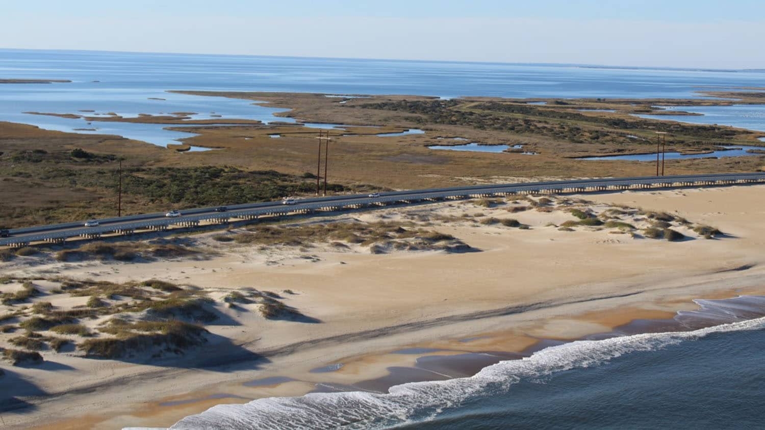 Aerial photograph of the ocean, beach, dunes, a highway, and then wetlands.