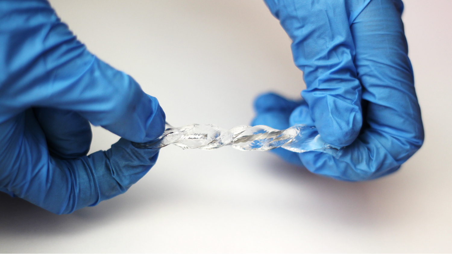Latex-gloved hands holding a clear hydrogel.