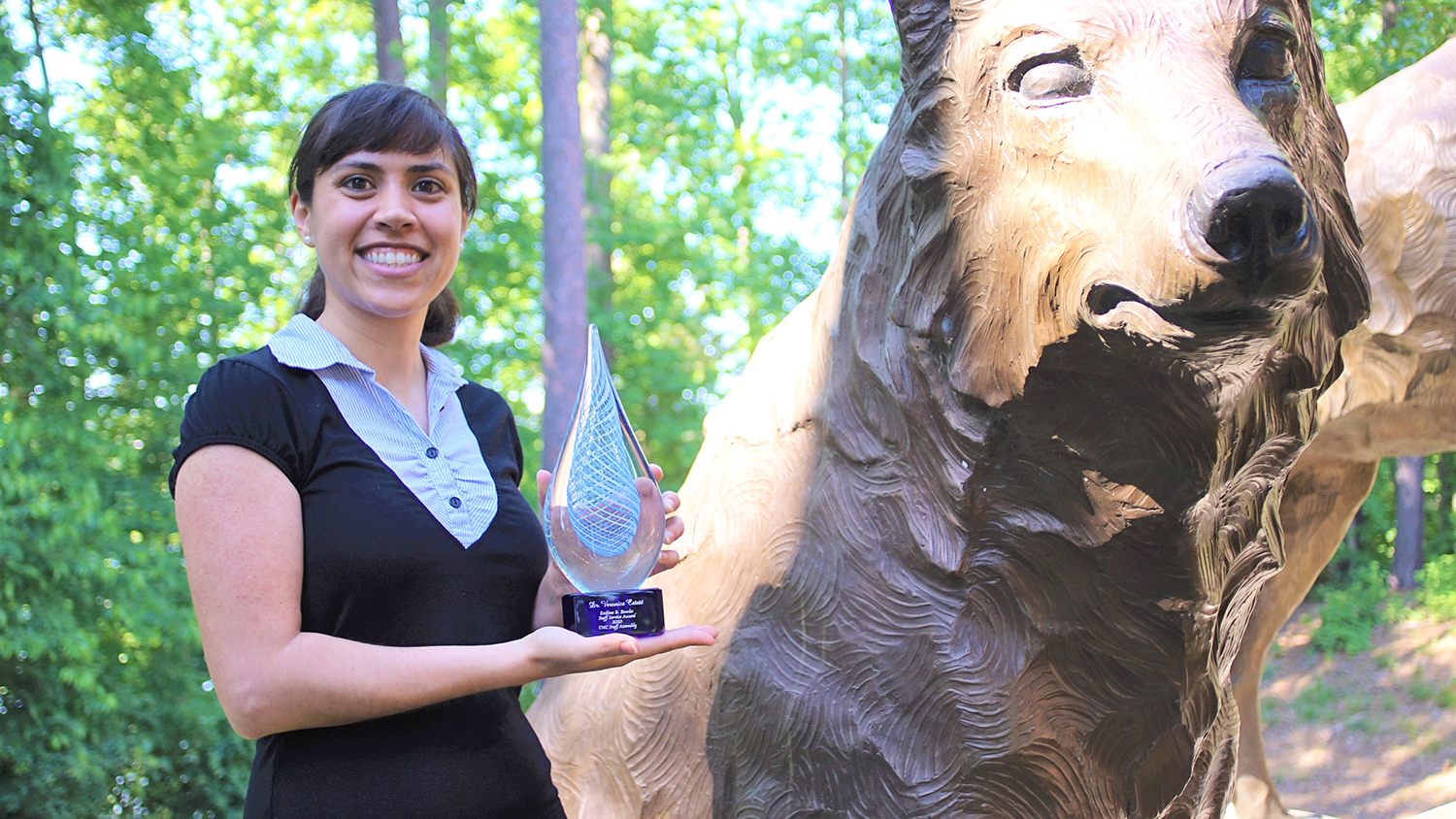 Veronica Cateté standing outside holding her award next to an sculpture of a wolf.