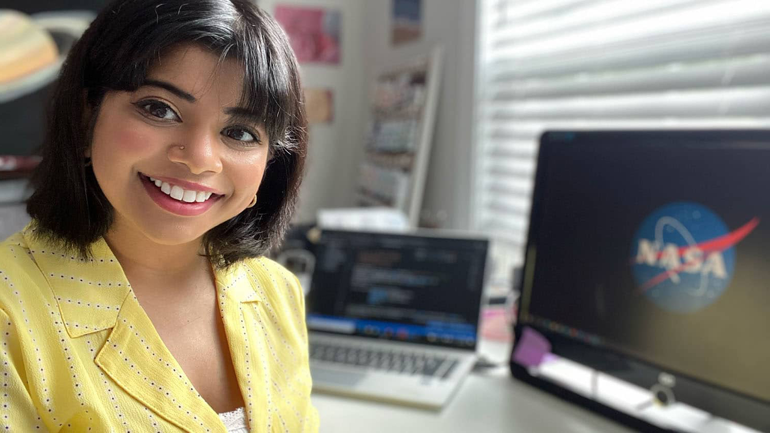 Shilpa Kancharla sitting at desk in front of computer screen displaying the NASA logo.
