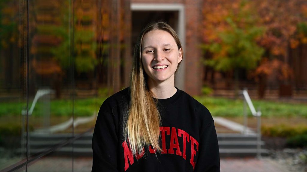 Georgia Burress in black NC State sweatshirt standing outside in sunlight.