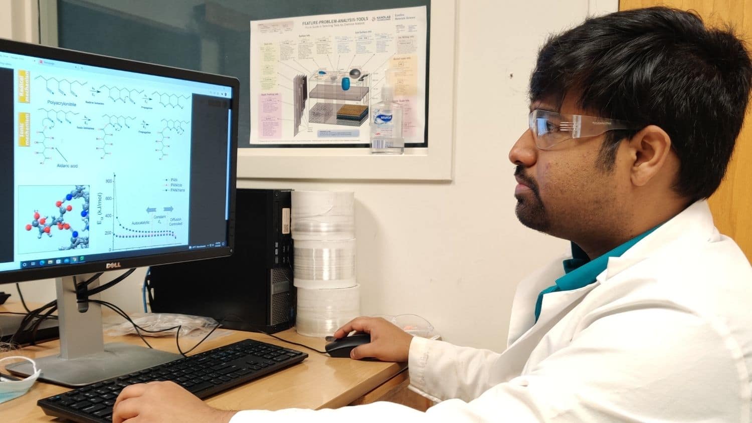 Researcher seated at desk looking at graphs and data on a computer screen.