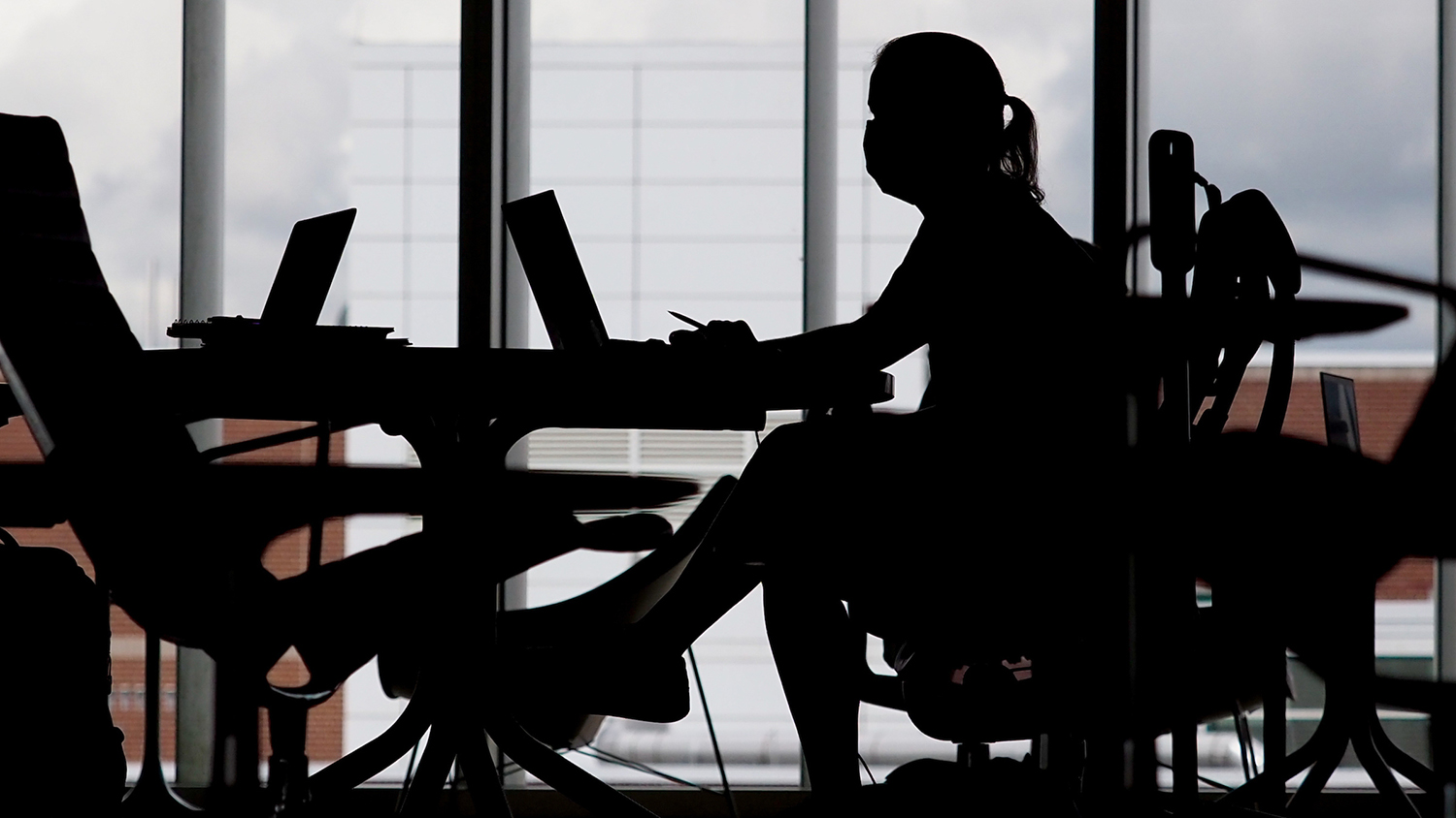Silhouette of woman at table working on a mobile computer.