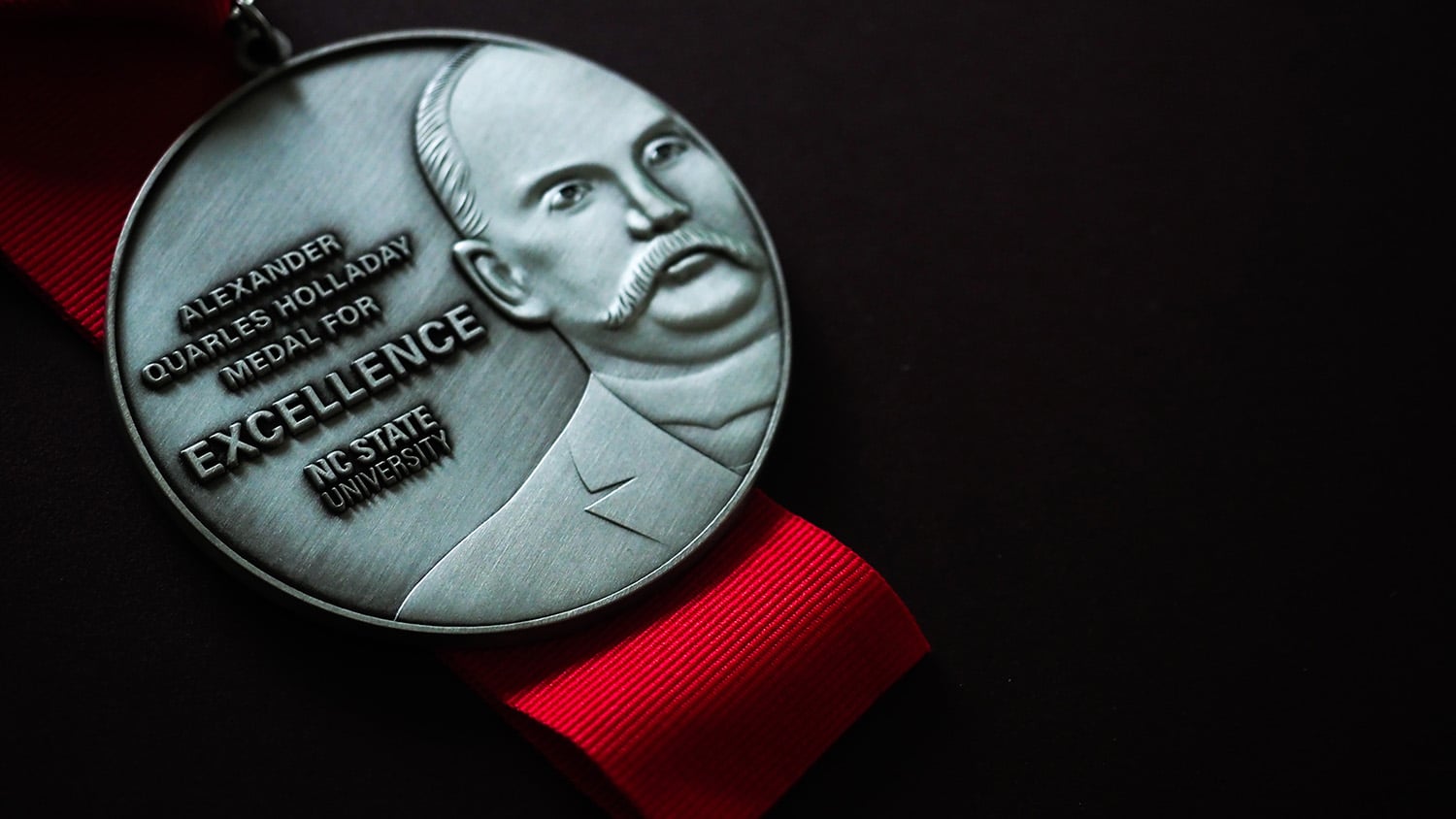 Silver Holladay medal with red ribbon on black background.