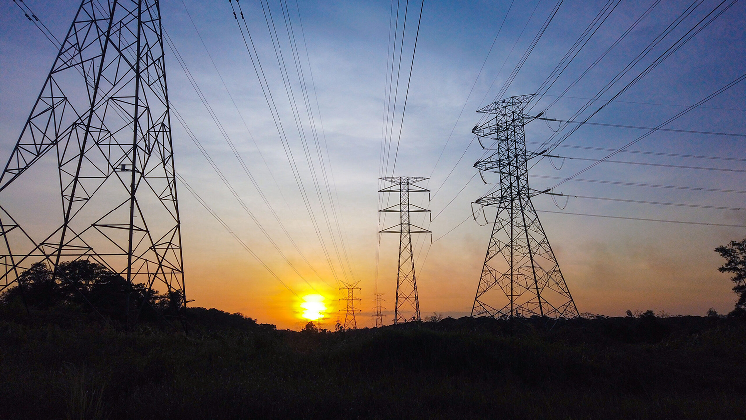 High tension powerlines and towers silhouetted by a sunset.