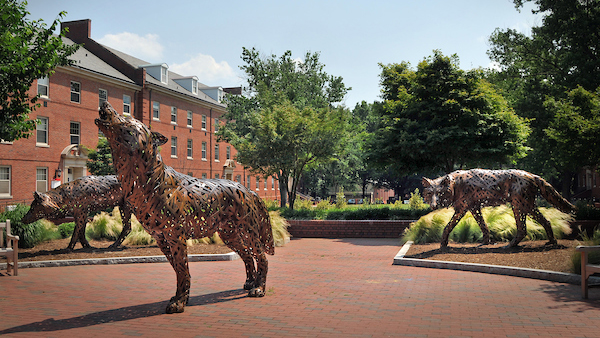 Bronze wolf statues amid brick-paved area and landscaping.