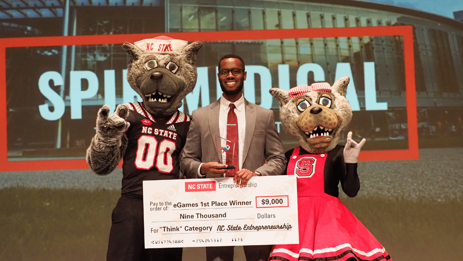 eGames winner poses holding a check with Mr. and Mrs. Wuf.