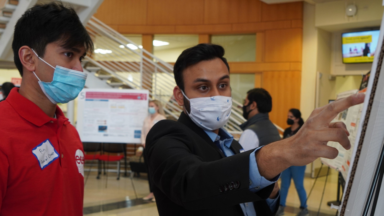 Jishnudeep Kar pointing to poster while explaining project to fellow student.