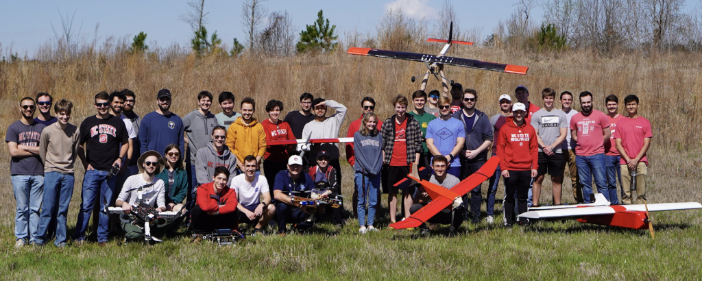 Aerospace engineering students pose for a large group photo in grassy field.