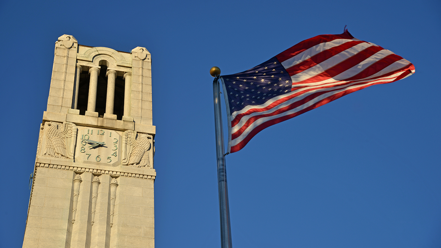 NC State belltower and US flag in early morning light.