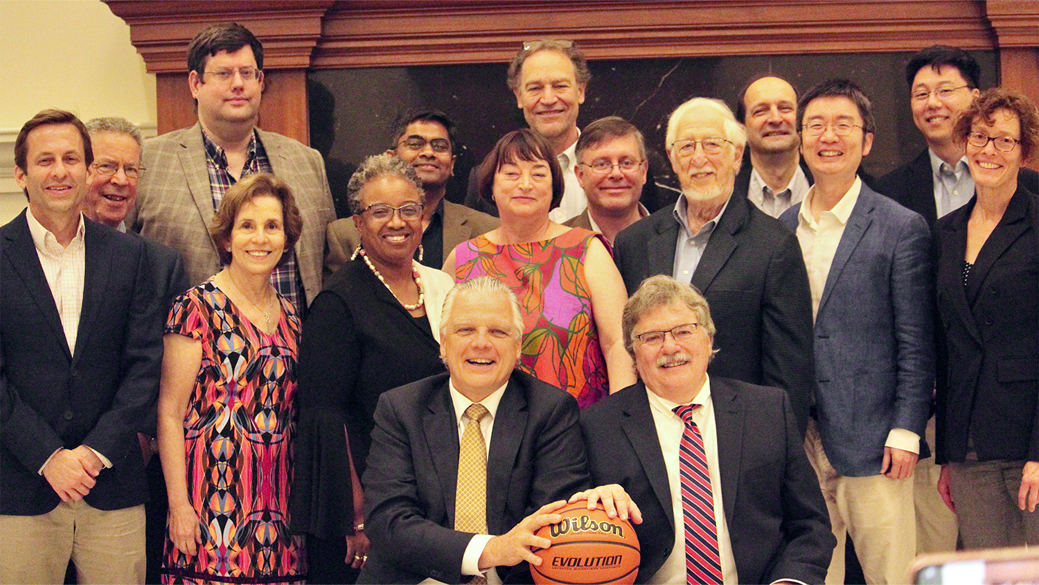 A group of faculty pose with Professors Peretti and Lamb while they hold a basketball.