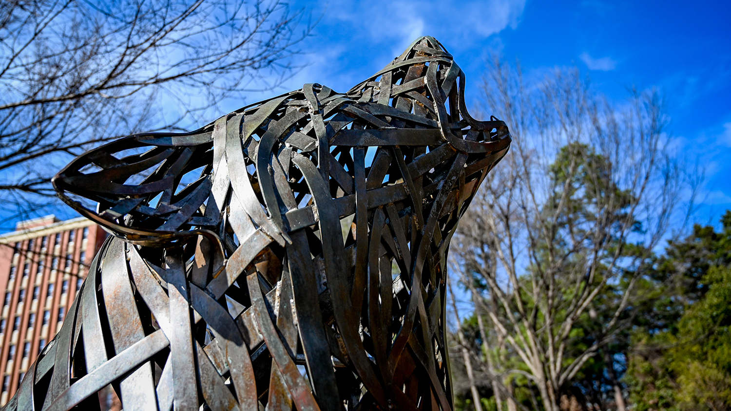 Howling wolf sculpture silhouetted by blue sky.