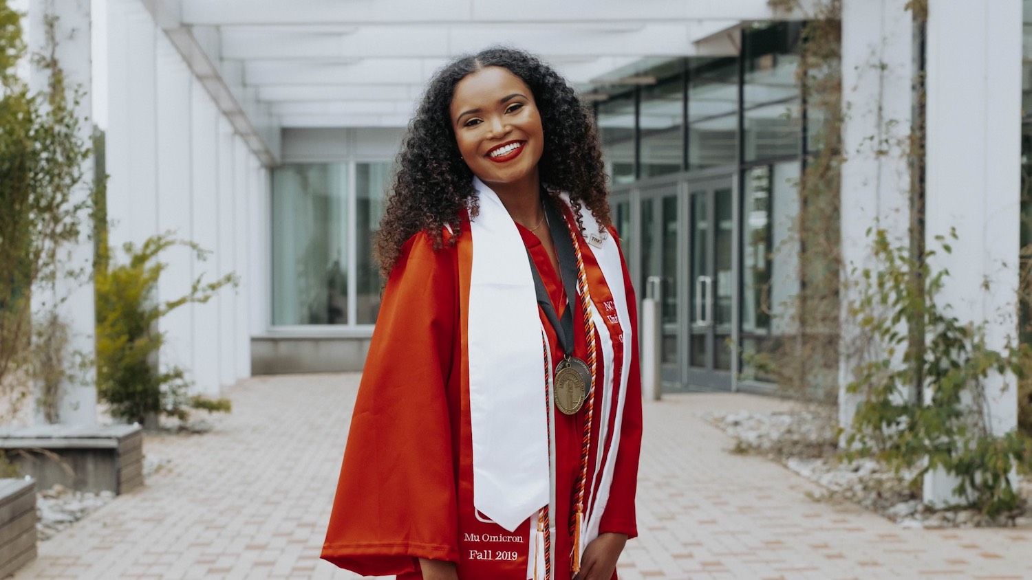 Solteria Ross poses in graduation gown in front of Hunt Library.