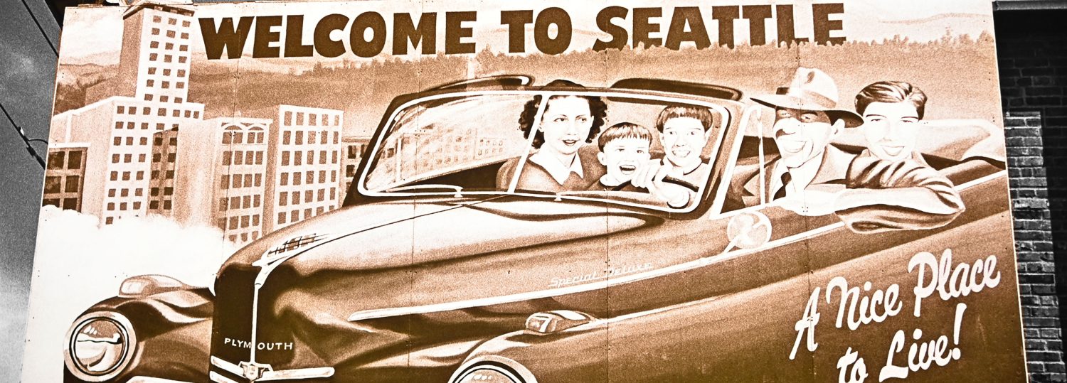 A retro-style billboard showing 1950s era family in a convertible with mother and father in front and children in the back. Text on sign states "Welcome to Seattle".