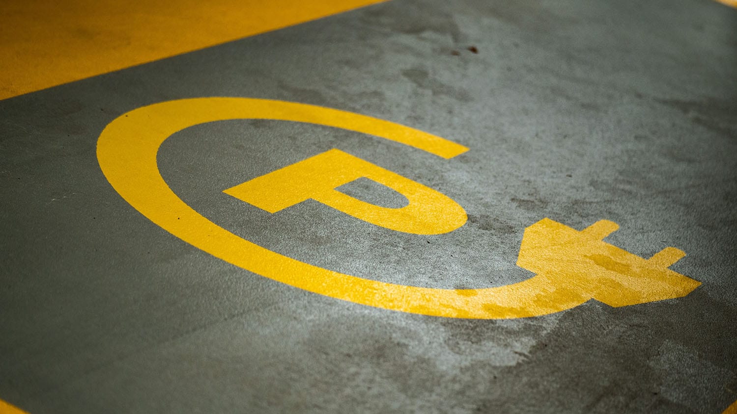 Yellow logo painted on black asphalt showing where to park electric vehicle for charging station.
