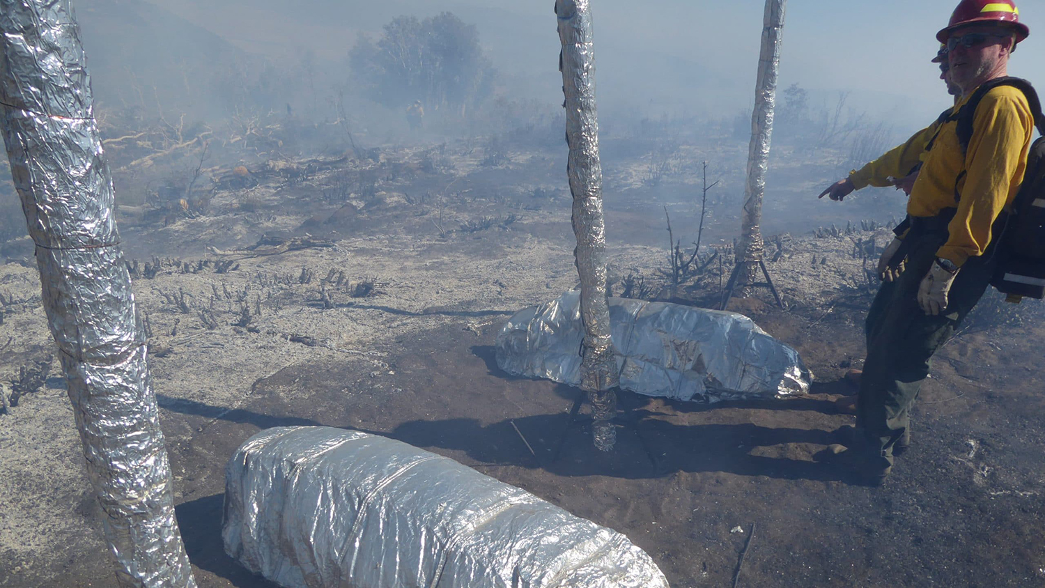 Firefighter points to two fire shelters being demonstrated in use in a burned out natural area.