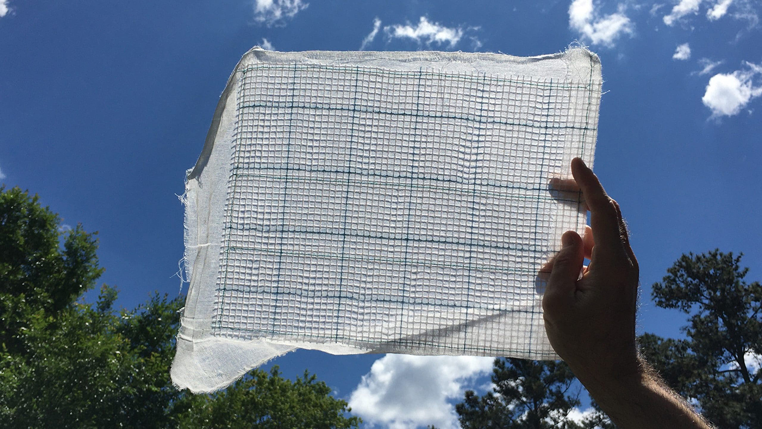 A white-colored textile filter being held up to the sky to show the texture and thinness of the material.