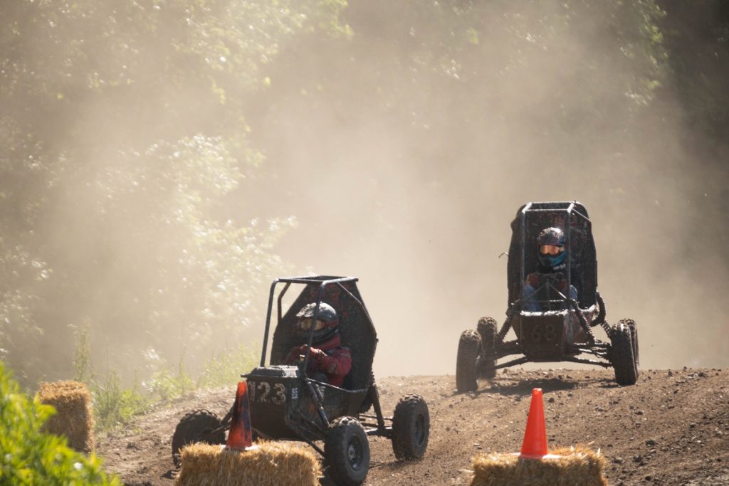 NC State University Pack Motorsports Baja SAE Team vehicle racing another vehicle on a dusty dirt track.
