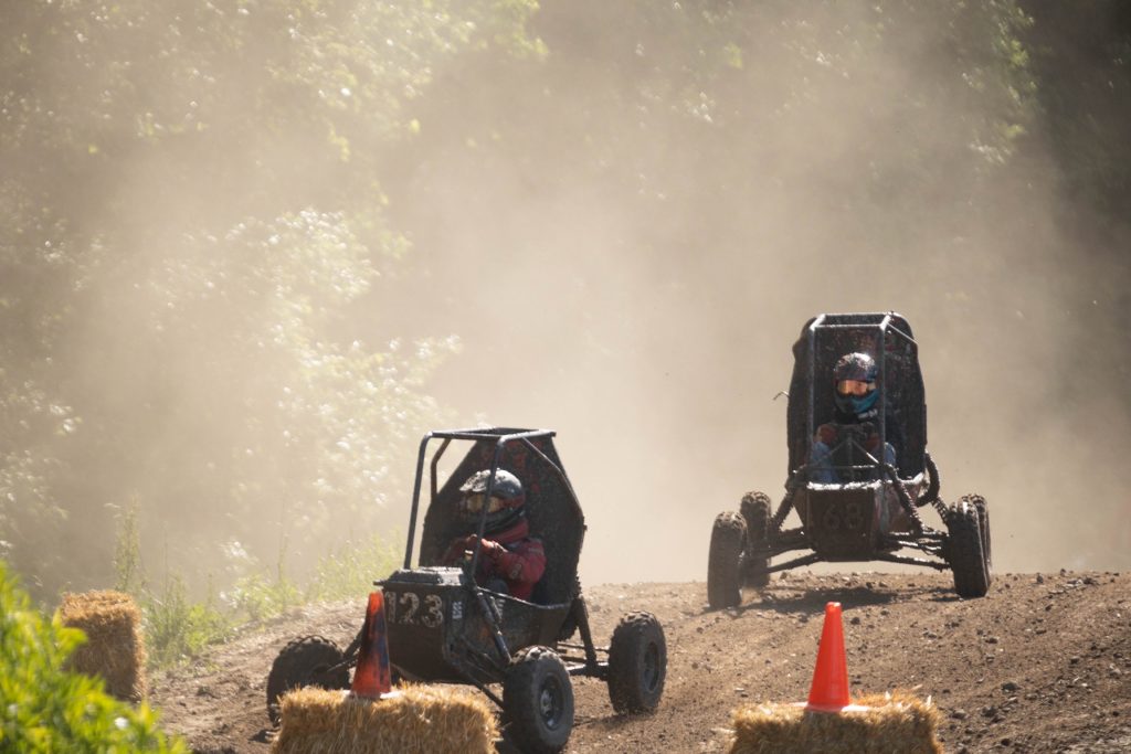 NC State University Pack Motorsports Baja SAE Team vehicle racing another vehicle on a dusty dirt track.