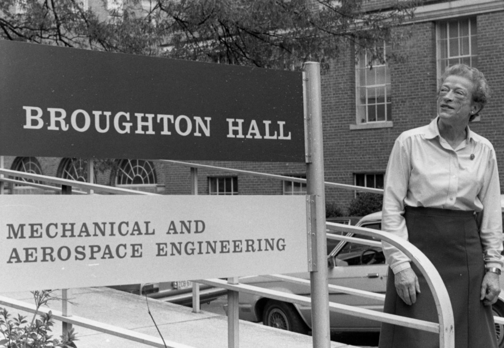 A black and white photo of Katherine Stinson standing next to sign for Broughton Hall.