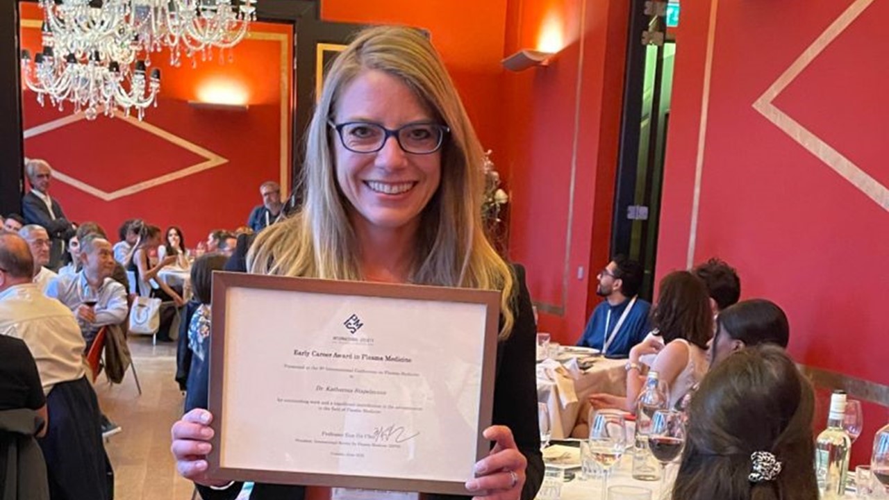 Dr. Katharina Stapelmann holding award certificate.