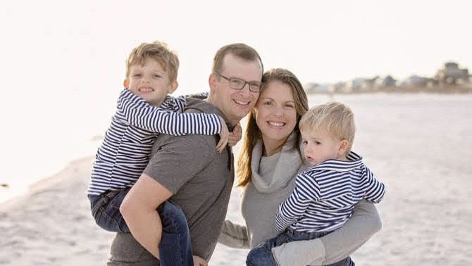 David Anderson, left and wife Allison each hold one of their two children while standing on the beach.