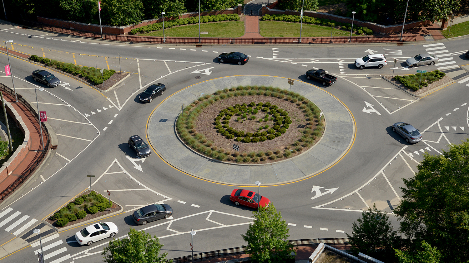 An aerial view of several automobiles navigating a traffic circle on Hillsborough Street near the NC State campus.
