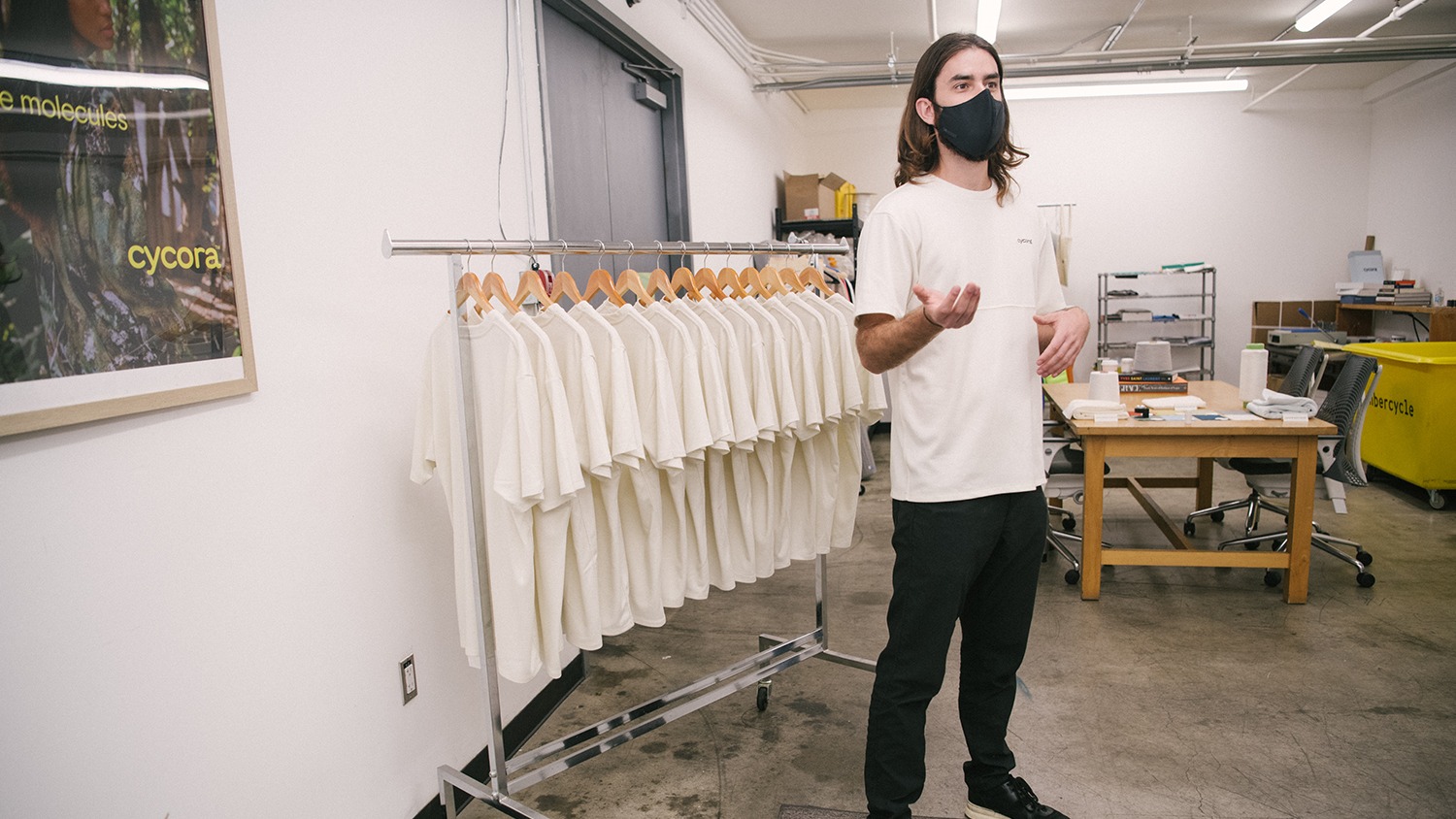 Matthew Iezzi dressed in white shirt and black pants standing in front of rolling rack of hanging clothes.
