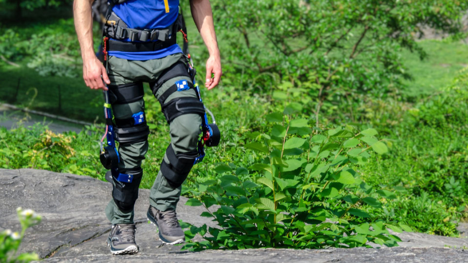 Person wearing an exoskeleton on legs while walking outside in a natural area.