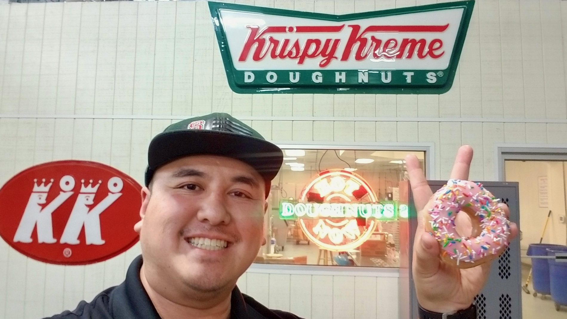 Jose Tan holds aloft a donut while standing in front of a Krispy Kreme wall sign.