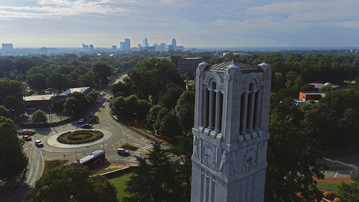 Aerial view of the NC State Belltower on main campus. The downtown Raleigh skyline is in the background.