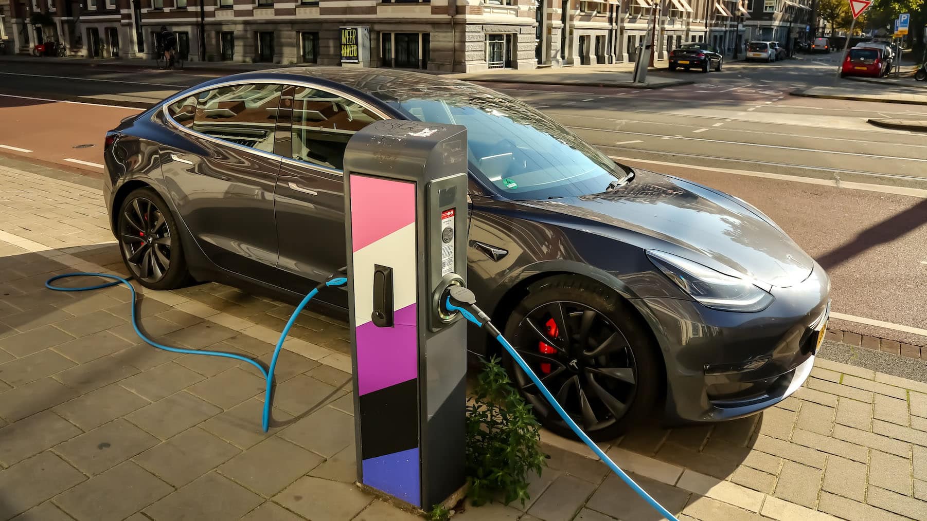 A dark grey, 4-door sedan electric vehicle connected to a charging station.