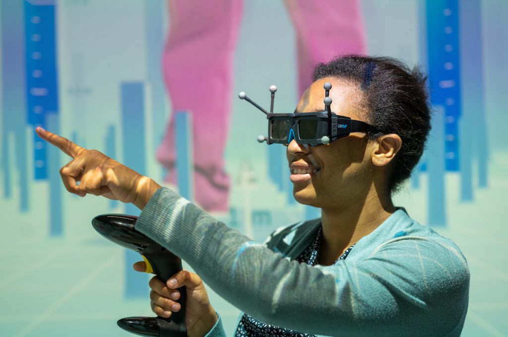 African-American female student wearing a virtual reality headset and holding a handheld controller.