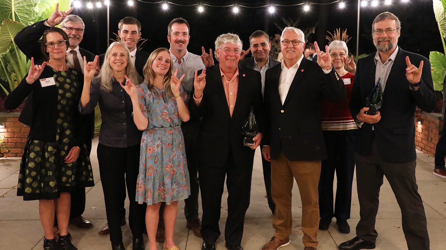 Members of the College of Agriculture's Sweetpotato Breeding and Genetics Program pose with Chancellor Randy Woodson, holding up the "wolf" hand sign.