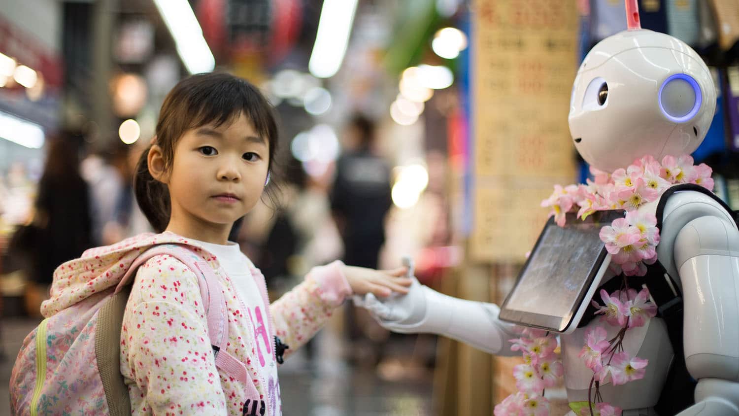 A young girl of East Asian descent touches hands with a robot.