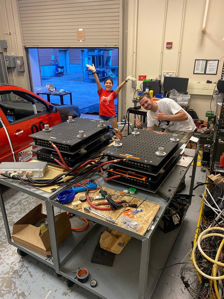 Two NC State students work on the SolarPack garage in the middle of a garage full of tools and auto equipment.