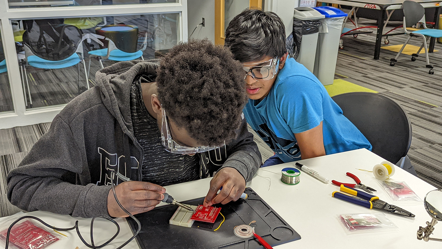 Two students at lab work table soldering electronics.