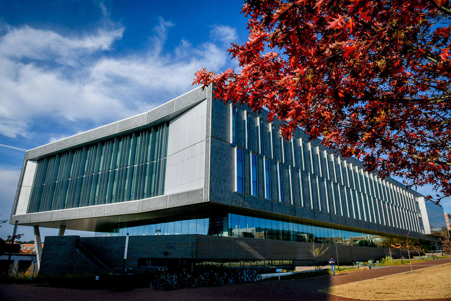 Fitts-Woolard Hall in the fall. Red leaves show in the upper right hand corner and blue sky and clouds in the upper left corner.