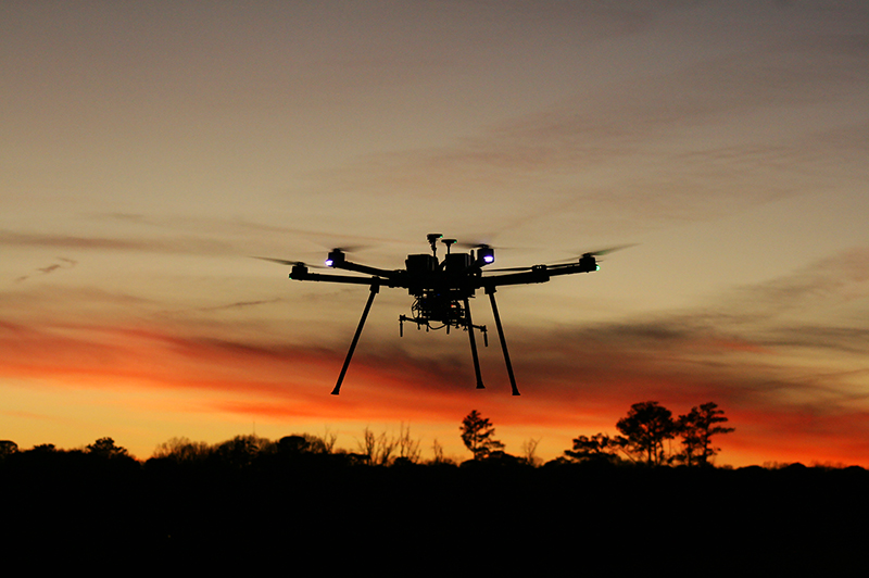 Aerial drone silhouetted against an orange sunset.